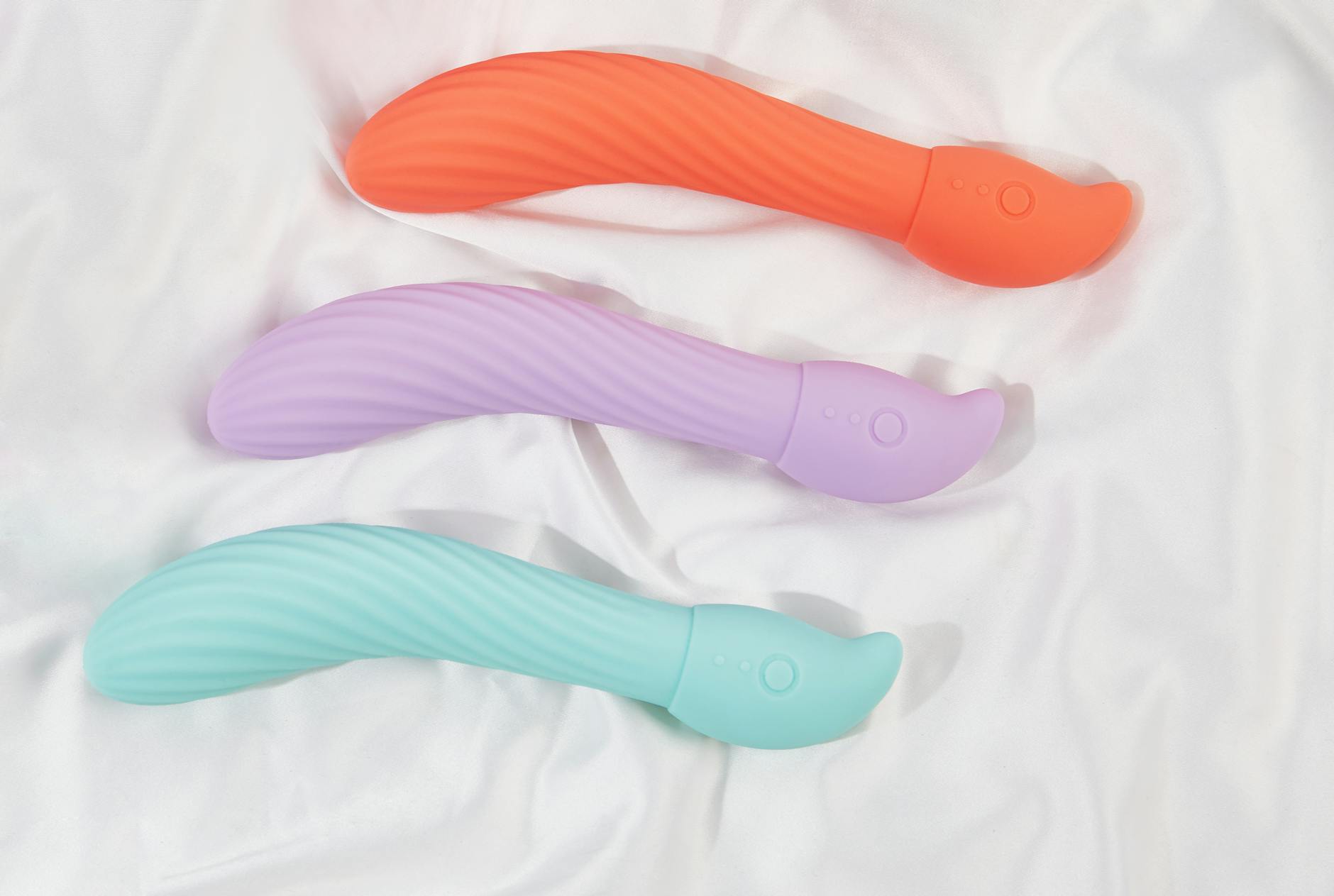A teal silicone vibrator on smooth white silk fabric, emphasizing texture and tactile design