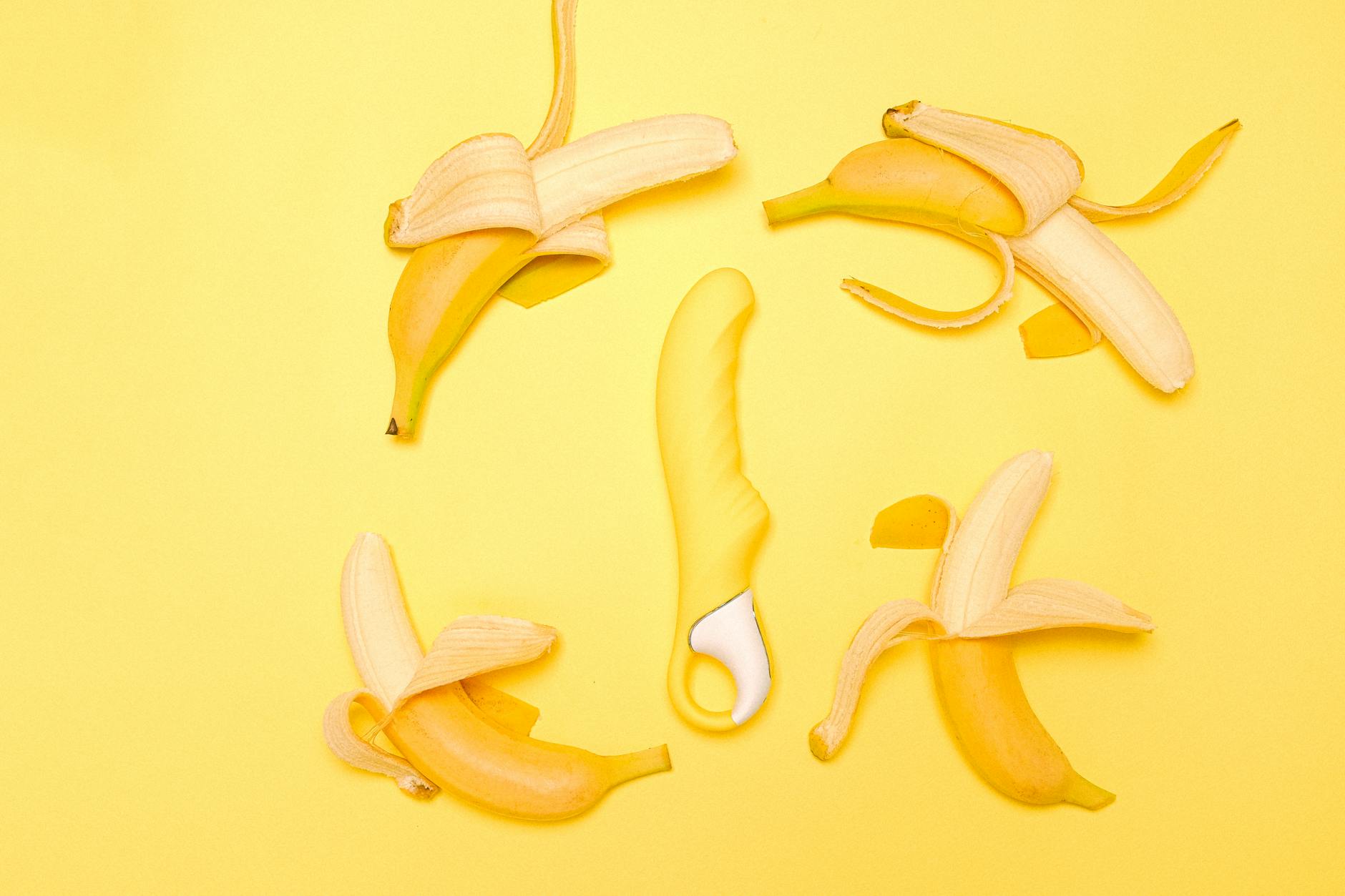 Yellow lemon-shaped silicone clitoral vibrator surrounded by fresh lemons on bright yellow background