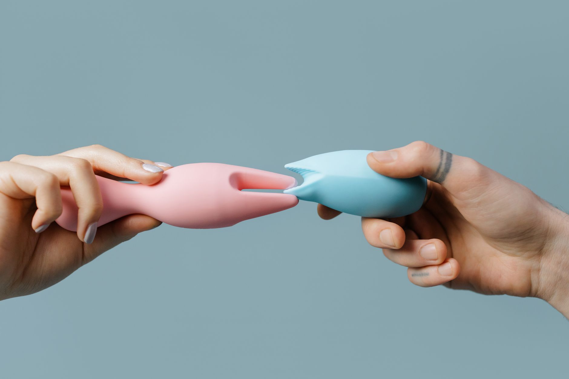 Close-up of hands holding a blue clitoral vibrator against a knitted sweater