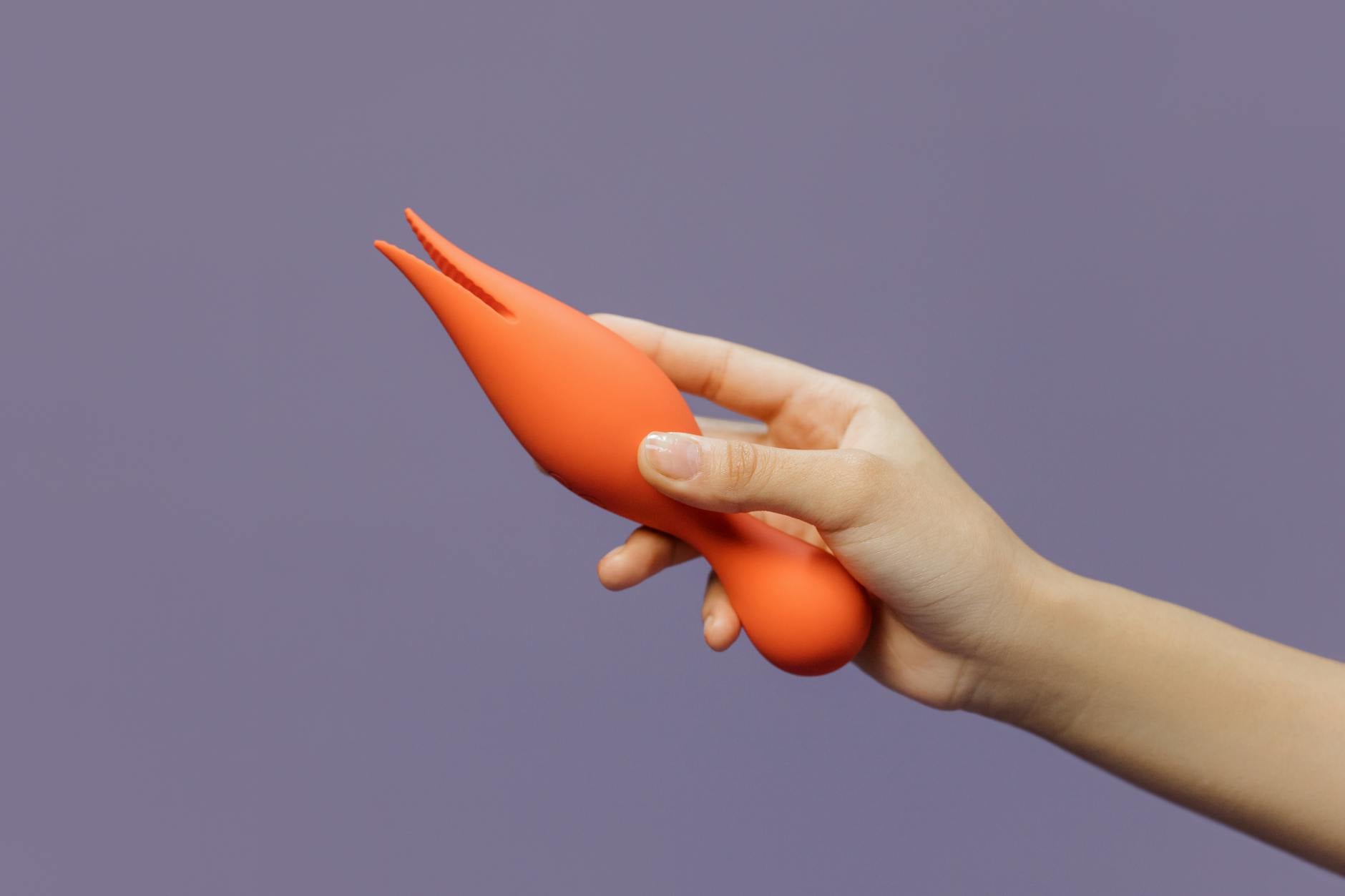 Hand holding an orange vibrator against purple backdrop