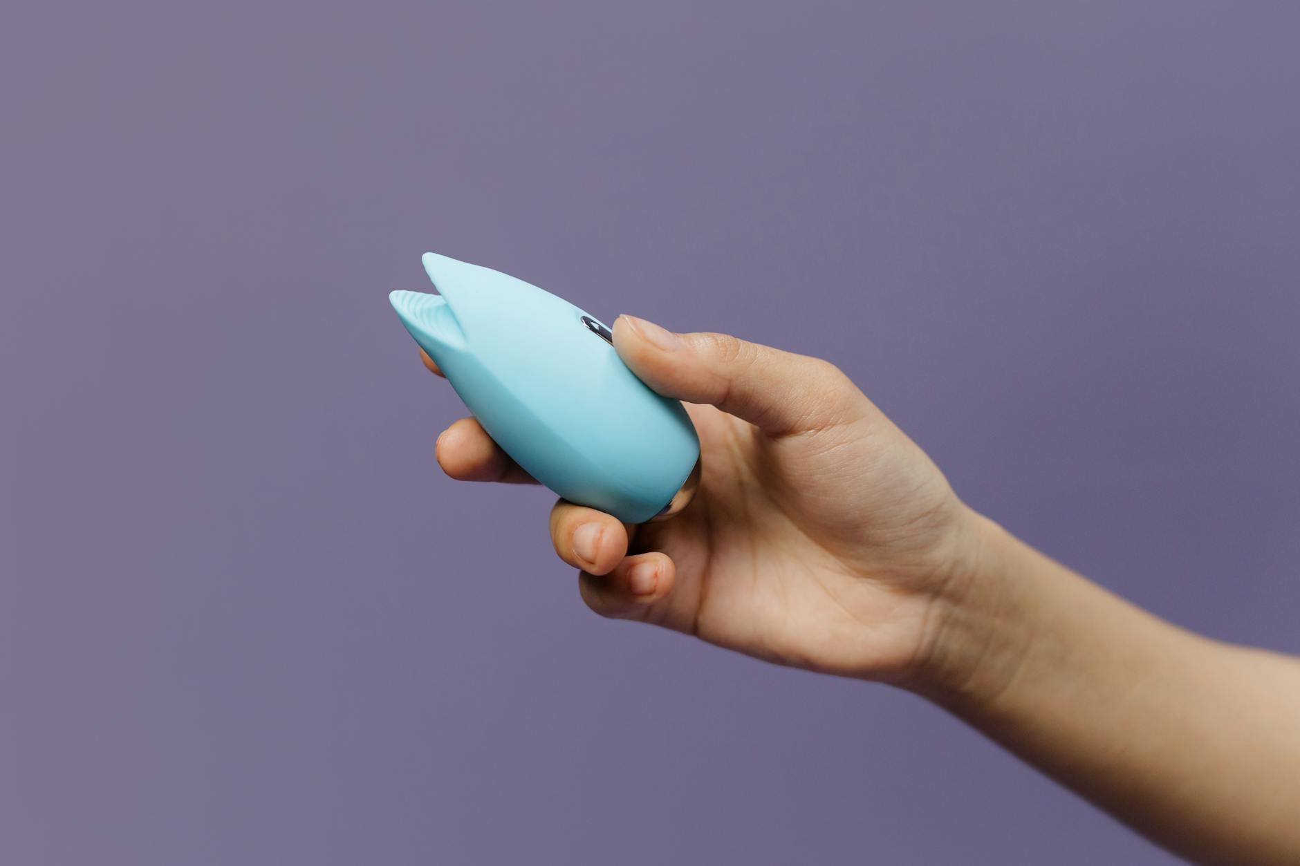 A blue silicone lemon vibrator held in hand against a solid purple background, promoting self-love and sexuality.
