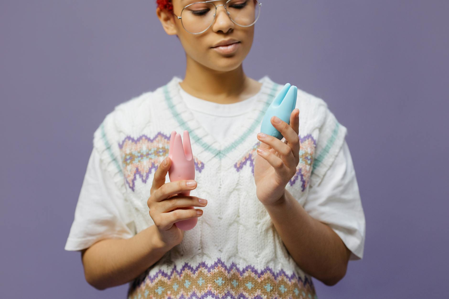 Woman holding a blue and pink silicone vibrator against a contemplative backdrop.